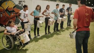 Foto de várias crianças e um professor fazendo aula de percussão no Projeto Tetear